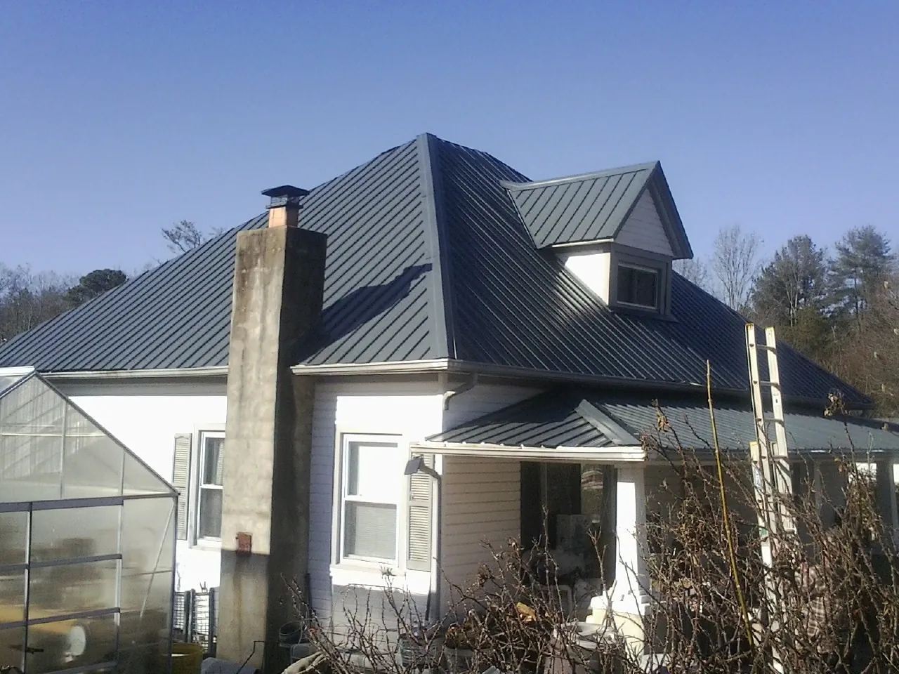 Dark blue standing seam metal roof on a white farmhouse with dormer — Slate & Tile Roof Repair by Roofing Brothers in Fort Pierre