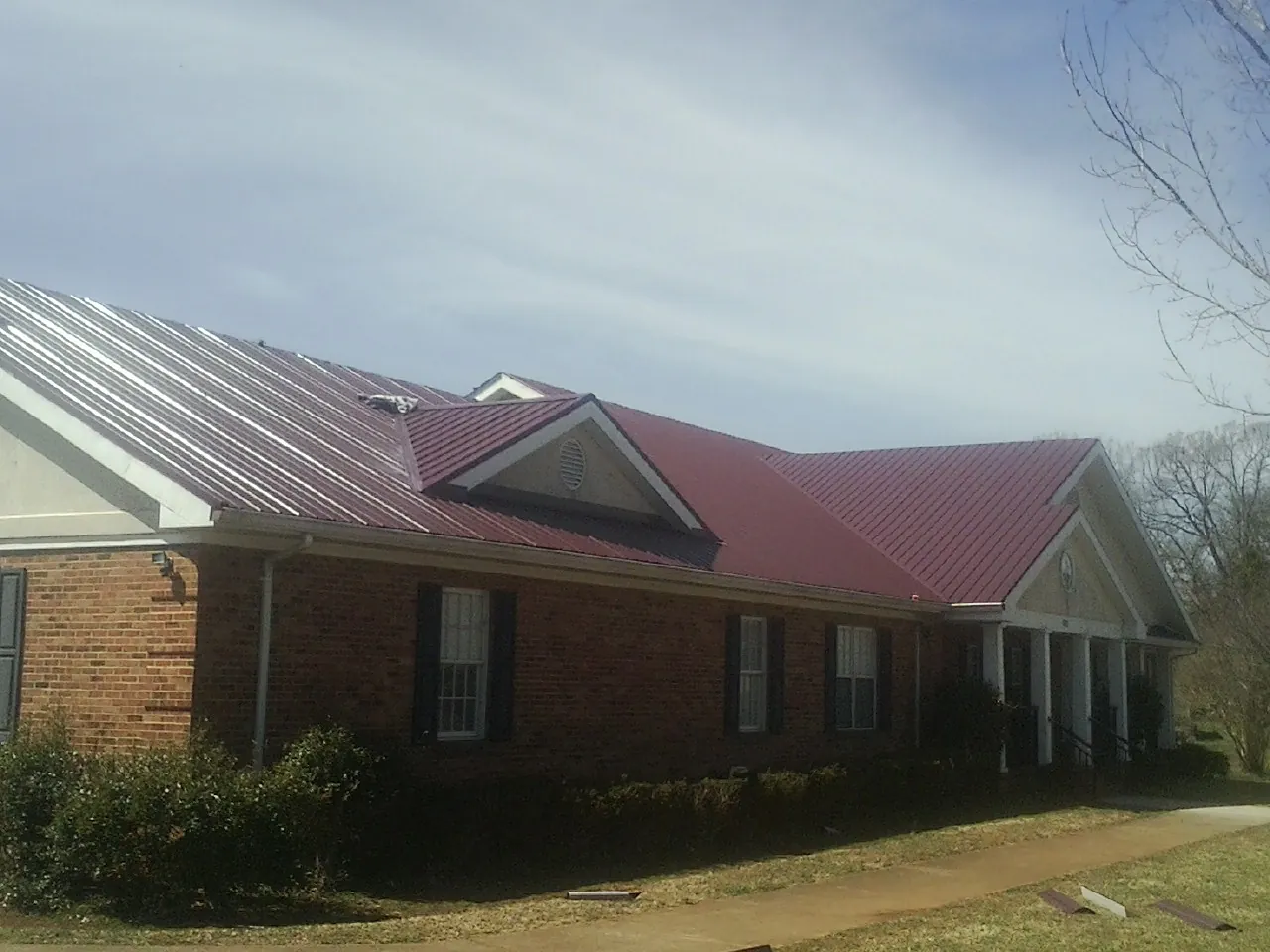 Red metal roof with gabled entries on a long brick building, from a Hail Damage Roof Repair job in Fort Pierre