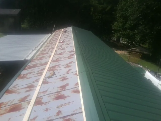 Old rusted panels beside newly installed green metal roofing — Wind Damage Roof Repair by Roofing Brothers in Fort Pierre