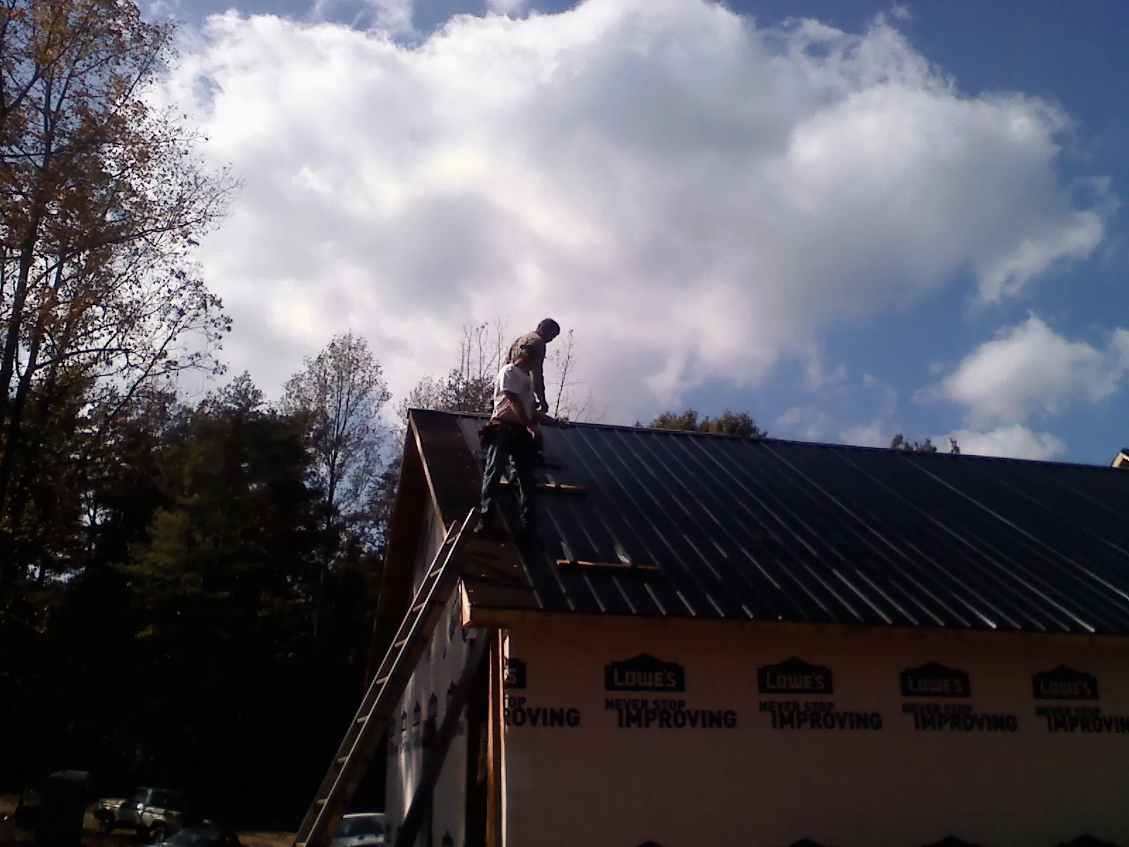 Roofer fastening dark metal panels high against a cloudy sky, from a Roof Inspection job in Fort Pierre