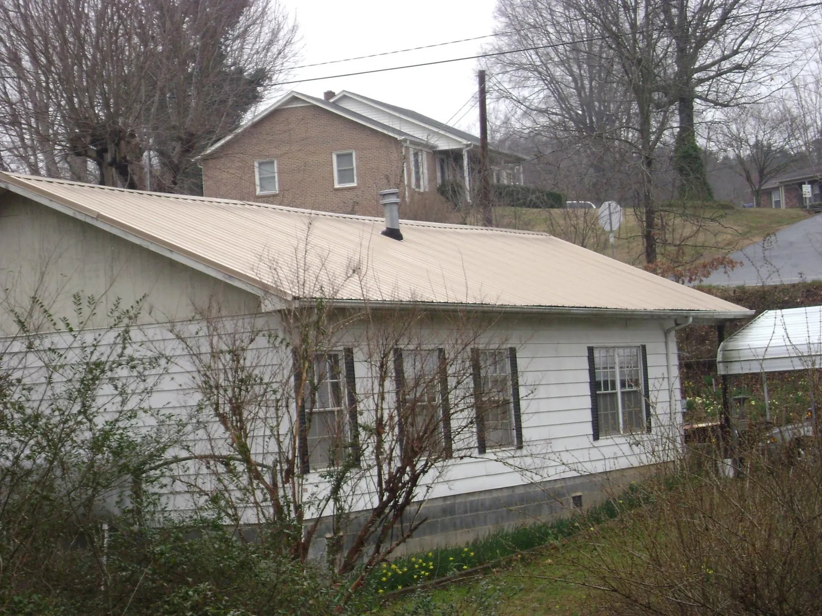 Tan metal roof on a white sided house set into a hillside — Commercial Roofing by Roofing Brothers in Fort Pierre